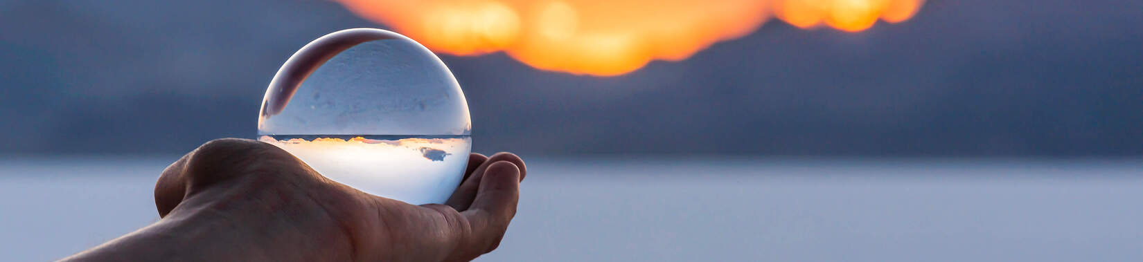 Eine Hand hält eine Glaskugel vor einem Sonnenuntergang